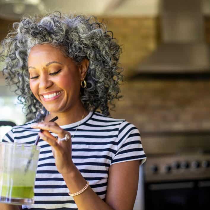 A beautiful black woman with white curly hair drinks coffee in her kitchen